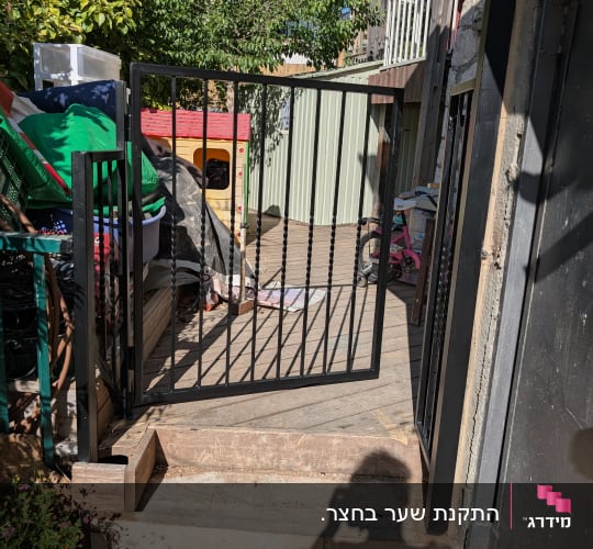 שער מתכת פתוח עם צל של אדם על המדרכה